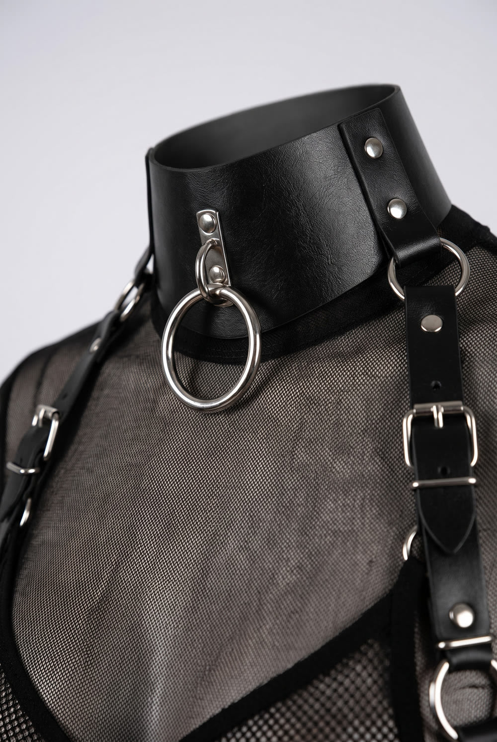 Close-up of the studded collar, silver O-ring and buckled shoulder strap of the structured cut-out body harness in black