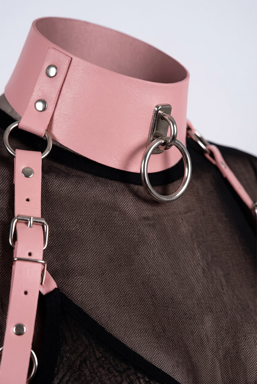 Close-up of the studded collar, silver O-ring and buckled shoulder strap of the structured cut-out body harness in pink