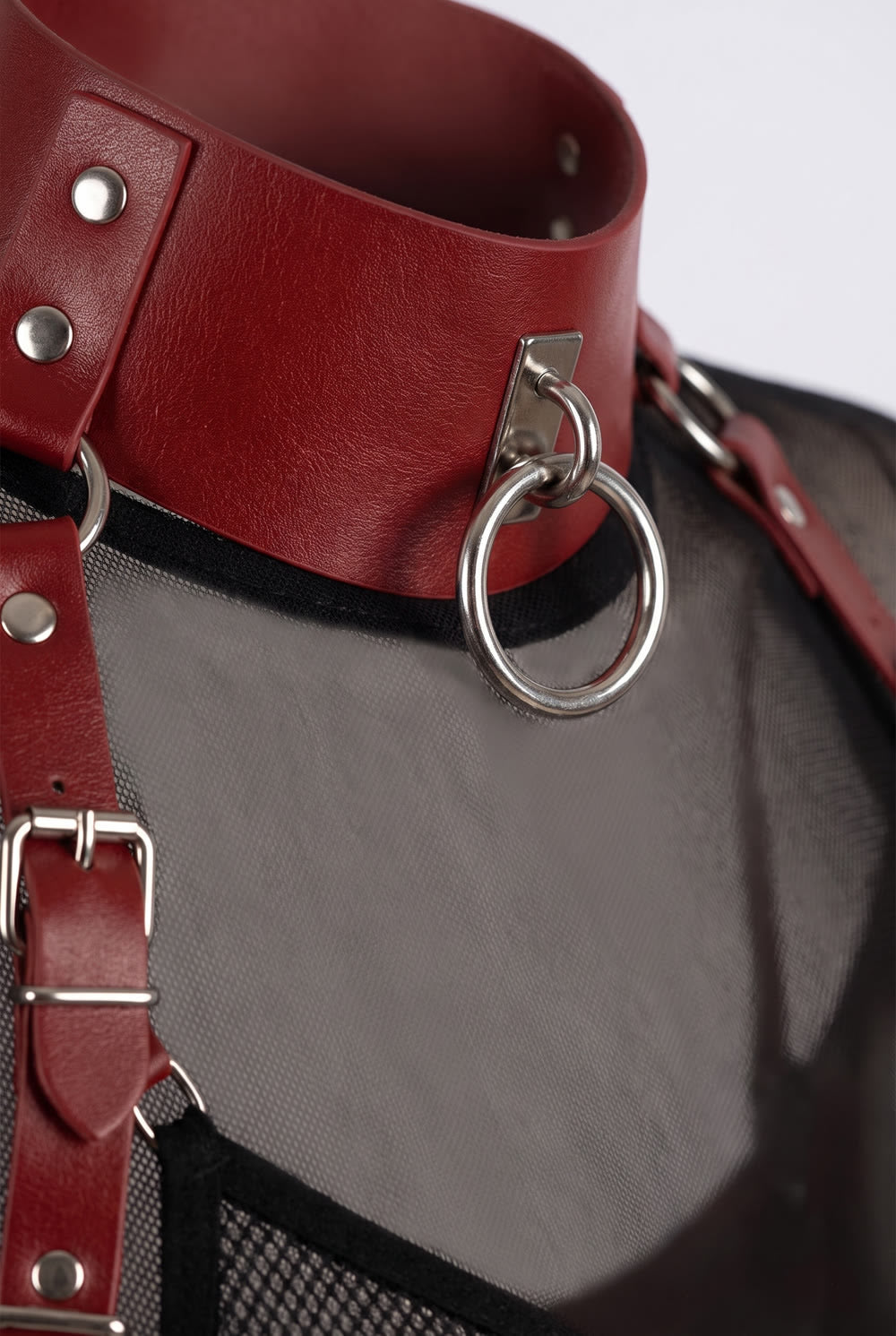 Close-up of the studded collar, silver O-ring and buckled shoulder strap of the structured cut-out body harness in red
